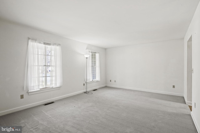 empty room featuring a wealth of natural light, visible vents, carpet flooring, and baseboards