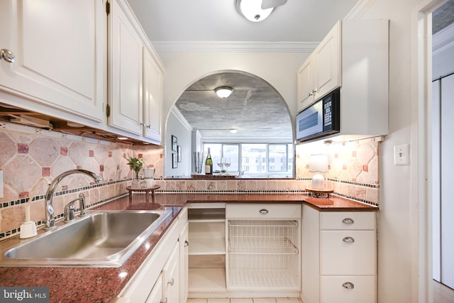 kitchen featuring crown molding, dark countertops, white cabinetry, and a sink