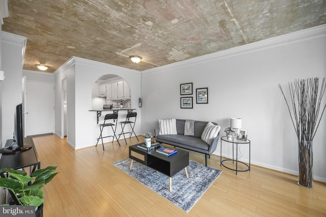 living room with arched walkways, ornamental molding, light wood-type flooring, and baseboards