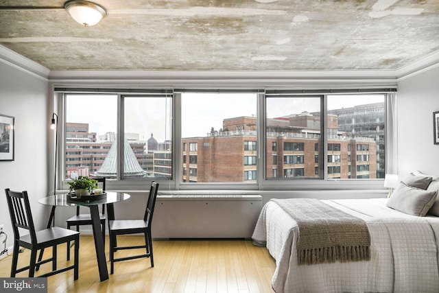 bedroom featuring ornamental molding, multiple windows, a city view, and light wood finished floors