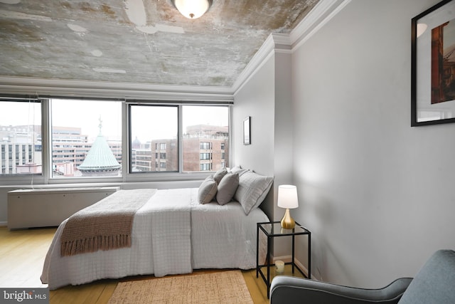 bedroom with a view of city, ornamental molding, and wood finished floors