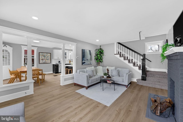 living room featuring a fireplace, recessed lighting, light wood-type flooring, baseboards, and stairs