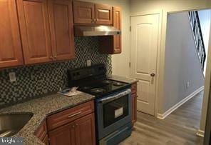 kitchen with light wood-style flooring, backsplash, stone countertops, black range with electric cooktop, and under cabinet range hood