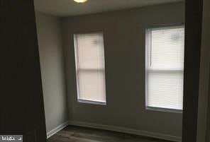 unfurnished room featuring dark wood-type flooring, plenty of natural light, and baseboards