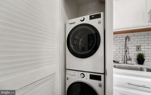 clothes washing area with stacked washer / drying machine, laundry area, and a sink