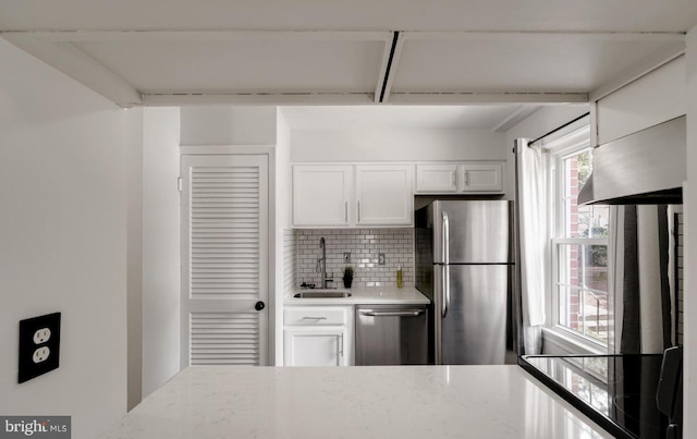 kitchen featuring light stone counters, a sink, white cabinets, appliances with stainless steel finishes, and decorative backsplash