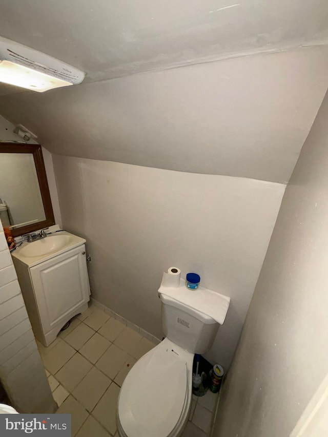 half bathroom featuring lofted ceiling, tile patterned flooring, vanity, and toilet