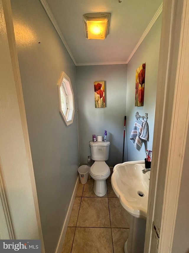 half bath featuring toilet, ornamental molding, a sink, baseboards, and tile patterned floors