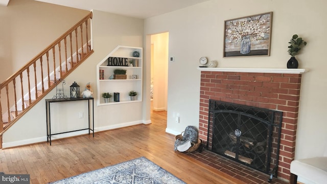 living area featuring stairs, a brick fireplace, hardwood / wood-style flooring, and baseboards