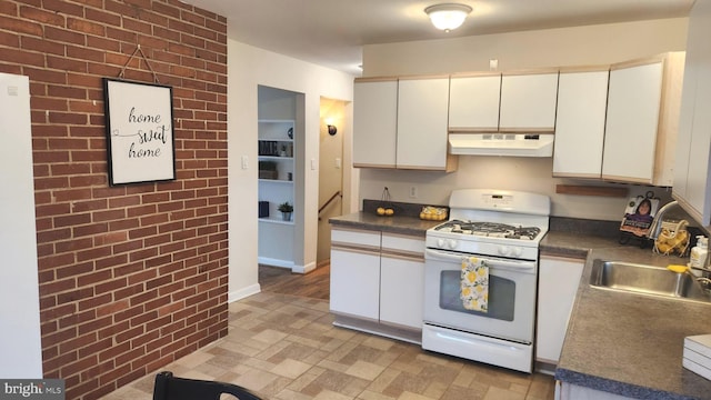 kitchen with gas range gas stove, dark countertops, white cabinetry, brick wall, and under cabinet range hood