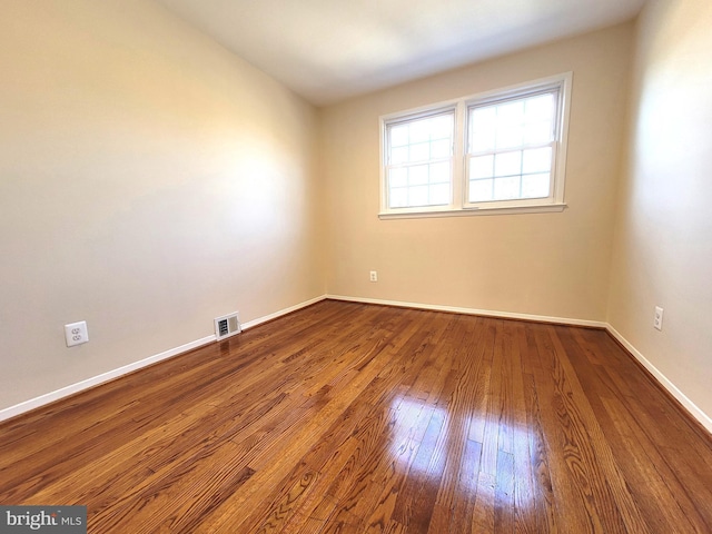 unfurnished room featuring wood-type flooring, visible vents, and baseboards