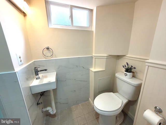 half bath with a wainscoted wall, a sink, tile patterned flooring, and toilet