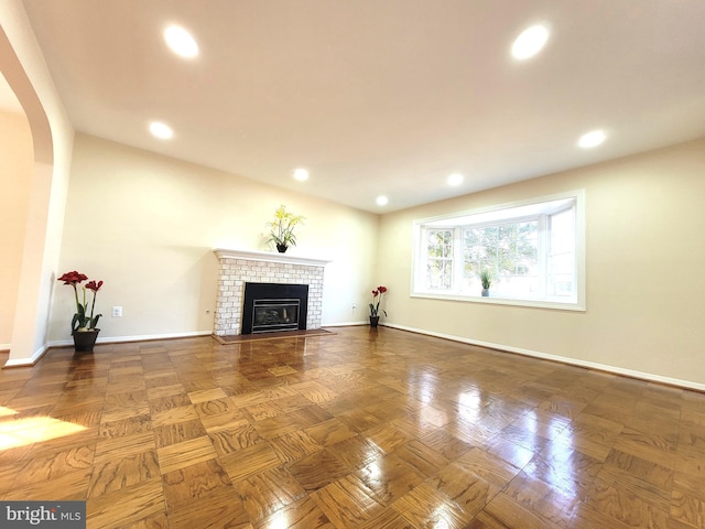 unfurnished living room with arched walkways, a brick fireplace, baseboards, and recessed lighting