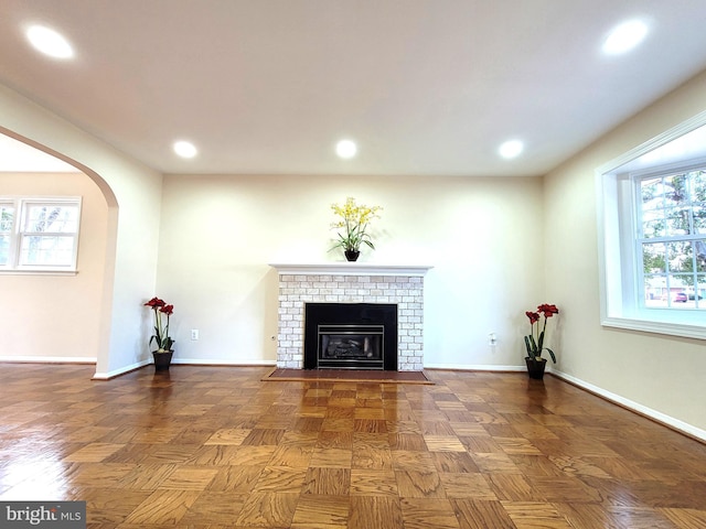 unfurnished living room with arched walkways, recessed lighting, a brick fireplace, and baseboards