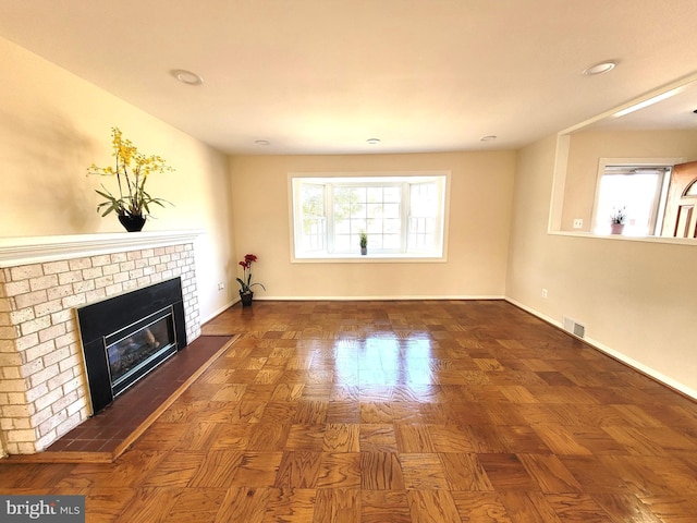 unfurnished living room with a brick fireplace, baseboards, and visible vents