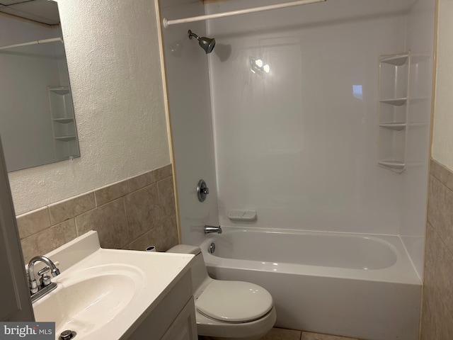 full bathroom with toilet, tub / shower combination, vanity, and tile walls