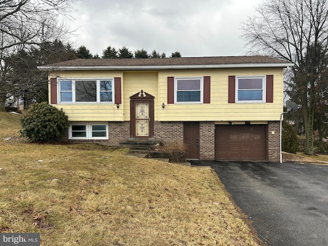 raised ranch featuring aphalt driveway, a front yard, brick siding, and a garage