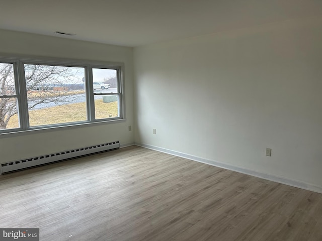 unfurnished room featuring a baseboard radiator, visible vents, baseboards, and wood finished floors