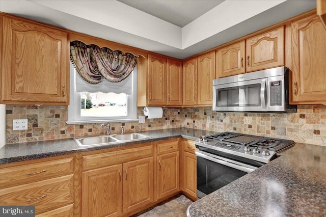 kitchen featuring appliances with stainless steel finishes, dark countertops, a sink, and tasteful backsplash