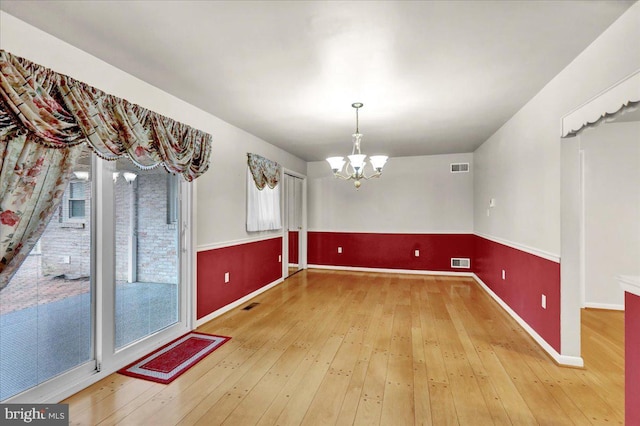 unfurnished dining area with hardwood / wood-style floors, visible vents, and an inviting chandelier