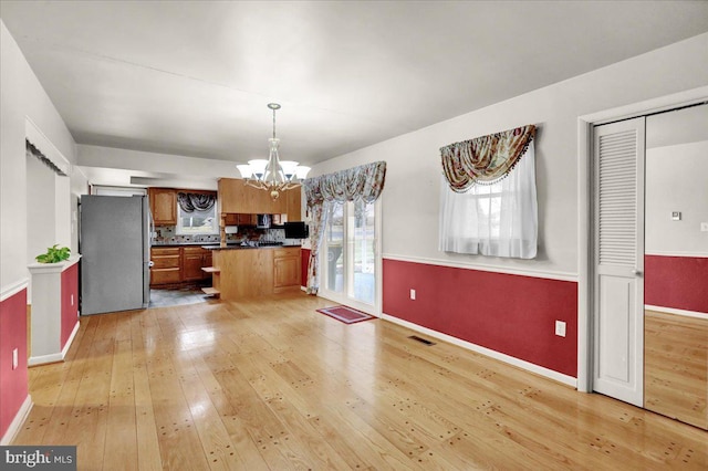 kitchen with visible vents, brown cabinets, freestanding refrigerator, an inviting chandelier, and light wood-style floors