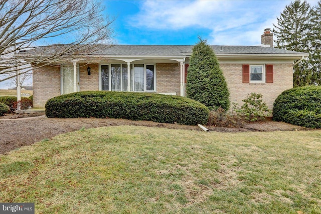 single story home with brick siding, a chimney, and a front yard