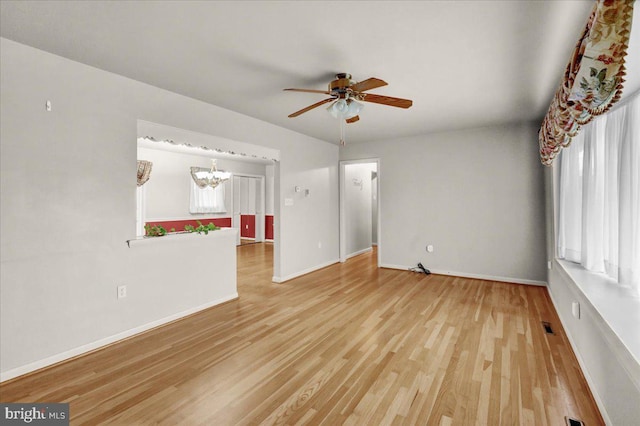 interior space featuring ceiling fan with notable chandelier, visible vents, baseboards, and wood finished floors