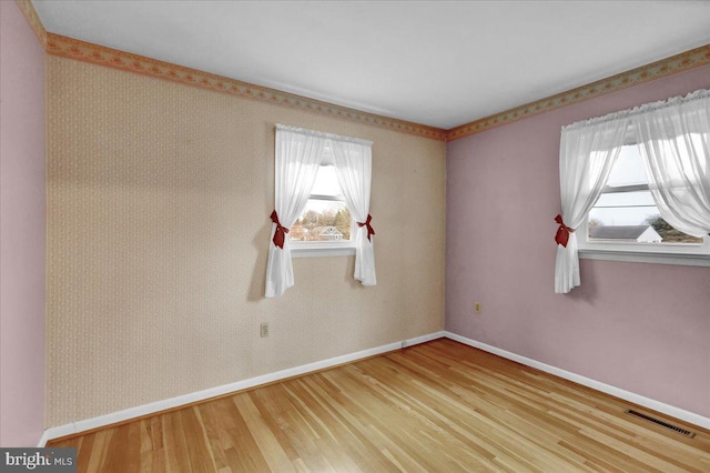 empty room featuring wallpapered walls, visible vents, baseboards, and wood finished floors