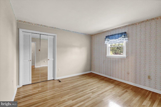 unfurnished room with light wood-type flooring, wallpapered walls, and baseboards