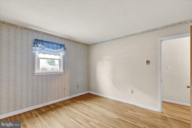 empty room with light wood finished floors, baseboards, and wallpapered walls