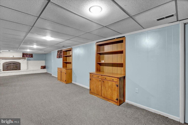 finished below grade area featuring a paneled ceiling, a brick fireplace, carpet flooring, and visible vents