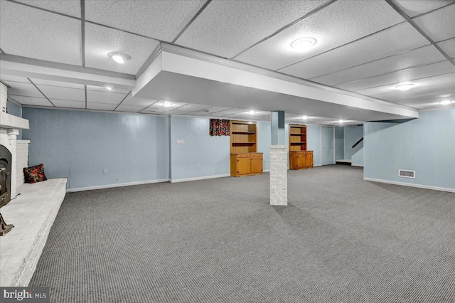 finished below grade area featuring carpet floors, a brick fireplace, visible vents, and baseboards