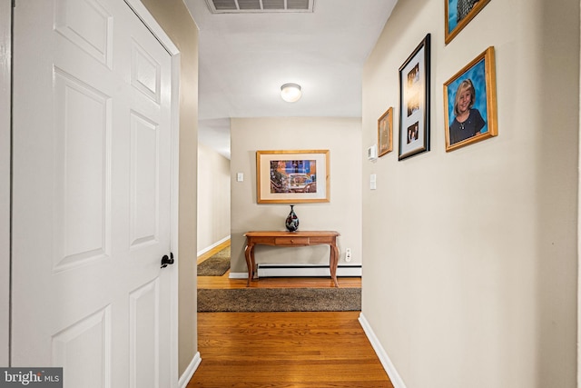 hall with a baseboard radiator, visible vents, baseboards, and wood finished floors