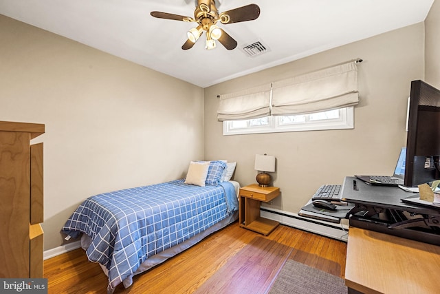 bedroom featuring a baseboard radiator, visible vents, baseboards, and wood finished floors