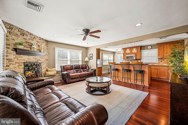 living area with visible vents, dark wood-style floors, ceiling fan, a stone fireplace, and recessed lighting