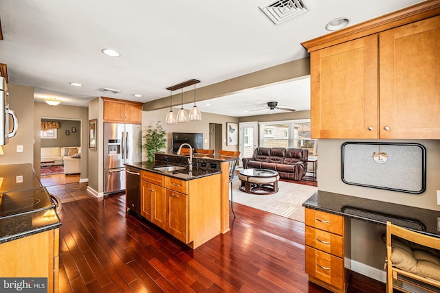 kitchen featuring stainless steel appliances, a sink, visible vents, open floor plan, and dark stone countertops