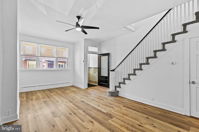 foyer entrance featuring a baseboard radiator, wood-type flooring, ceiling fan, baseboards, and stairs