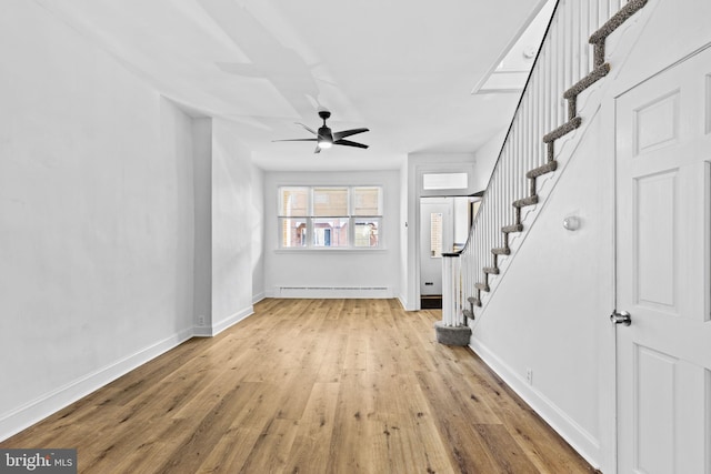 unfurnished living room featuring stairs, baseboard heating, wood finished floors, and baseboards