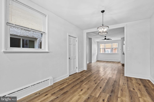 unfurnished dining area with ceiling fan with notable chandelier, hardwood / wood-style floors, baseboard heating, and baseboards