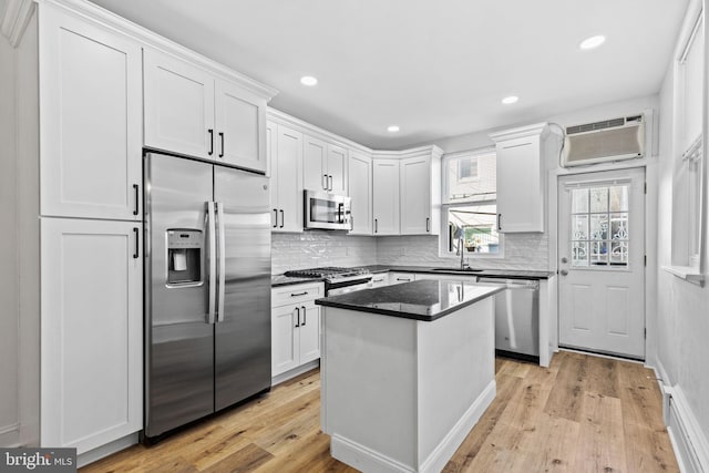 kitchen featuring stainless steel appliances, an AC wall unit, white cabinetry, and a sink