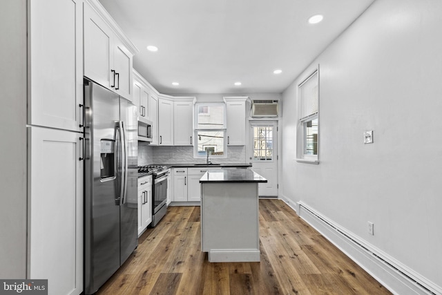 kitchen featuring white cabinets, dark countertops, a baseboard radiator, stainless steel appliances, and backsplash