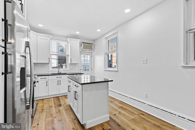 kitchen featuring stainless steel refrigerator with ice dispenser, dark countertops, a baseboard heating unit, an AC wall unit, and a sink