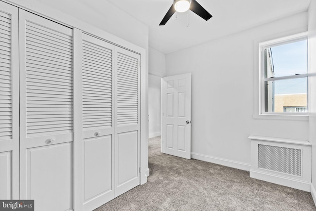 unfurnished bedroom featuring light carpet, baseboards, radiator heating unit, ceiling fan, and a closet