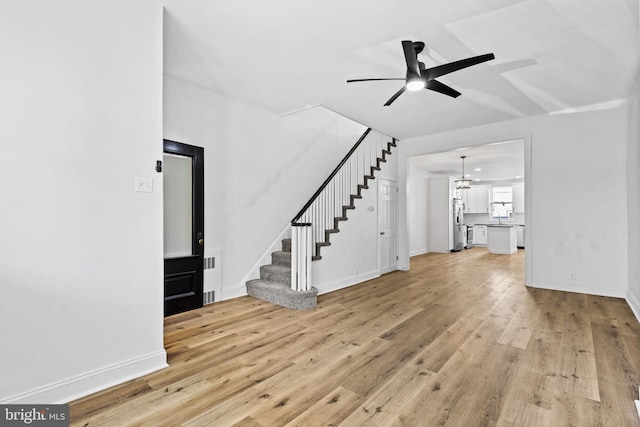 unfurnished living room featuring visible vents, baseboards, ceiling fan, stairway, and light wood-style floors