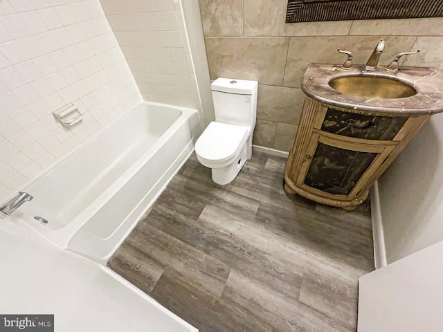 full bath with a bathing tub, toilet, a sink, wood finished floors, and tile walls