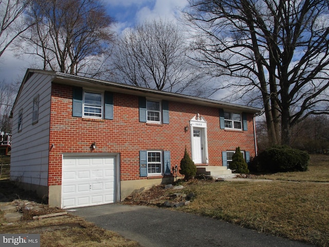 raised ranch featuring a garage, aphalt driveway, and brick siding