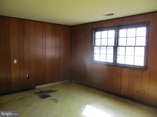 unfurnished room with light floors, visible vents, and wooden walls