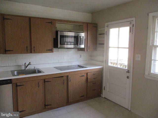 kitchen with appliances with stainless steel finishes, brown cabinets, a sink, light countertops, and backsplash