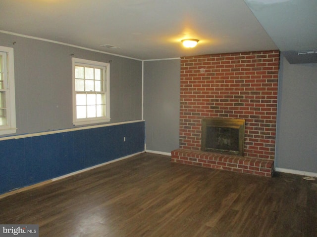 unfurnished living room with a brick fireplace, baseboards, ornamental molding, and wood finished floors