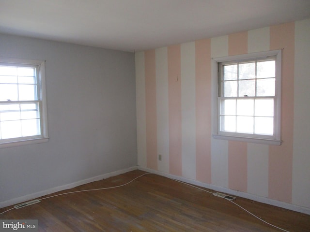 empty room featuring baseboards, wood finished floors, visible vents, and a healthy amount of sunlight